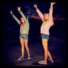 two girls are standing on their skateboards in the street at night with arms up