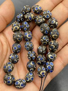 a hand holding a bunch of beads in it's palm, with blue and gold designs on them