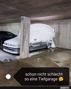 two cars are covered with snow in an underground parking garage, one is black and the other is white