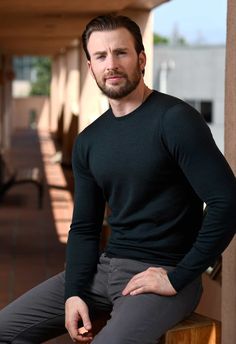 a man sitting on top of a wooden bench wearing a black shirt and gray pants