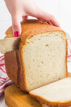 a loaf of white bread being cut by a person with a knife on a cutting board