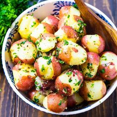 a bowl filled with potatoes and parsley on top of a wooden table