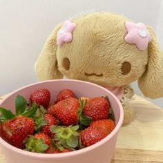 a pink bowl filled with strawberries next to a stuffed animal