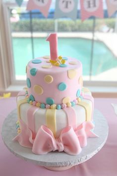 a pink cake with polka dots and a number one on it sitting on top of a table