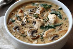 a close up of a bowl of soup with mushrooms and spinach on the side