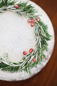 a cake decorated with greenery and pomegranates on a white plate