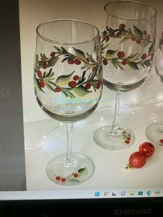 two wine glasses sitting next to each other on top of a computer screen with christmas decorations painted on them