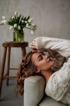 a woman laying on top of a couch next to a vase with flowers