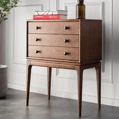 a wooden chest of drawers sitting next to a potted plant