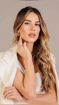 a woman with long hair wearing a white dress and gold earrings, posing for the camera