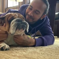 a man laying on the floor petting a brown and white bulldog's face