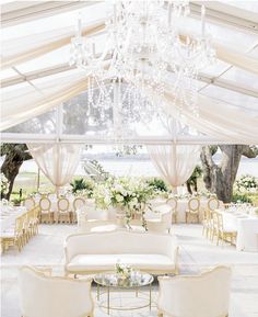 an elegant wedding reception with chandeliers and white couches under a tented area