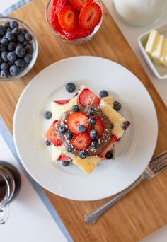 a white plate topped with cake covered in fruit next to milk and strawberries on top of a wooden cutting board