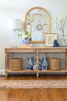 a table with baskets and vases on it in front of a mirror, framed by a gold frame