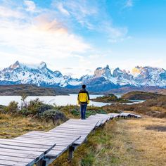 a man walking across a wooden bridge over a lake in front of snow covered mountains