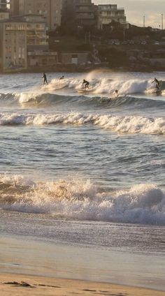 several surfers are riding the waves in front of some buildings on the shore line