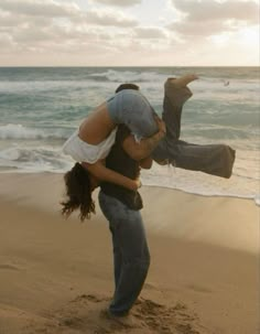 a man carrying a woman on his back while standing in the sand at the beach