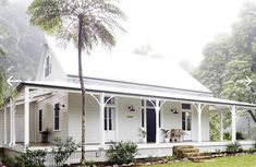 a white house with black shutters on the front porch and covered porch area, surrounded by palm trees