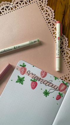 an open notebook with strawberries on it next to a pink pen and crochet doily