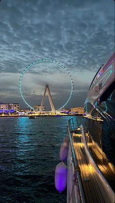 the ferris wheel is lit up at night over the water with buildings in the background