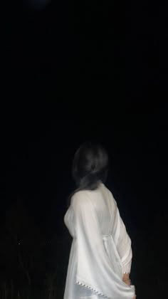 a woman in white is walking through the grass at night with her back turned to the camera