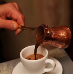 a person pours coffee into a white cup on a saucer with a wooden spoon