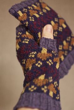 a hand holding up a purple and gold knitted mitt with flowers on it