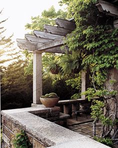 a stone bench sitting under a pergoline covered roof next to a lush green forest