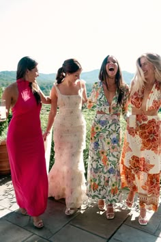 four women in dresses laughing and standing on a stone walkway with mountains in the background