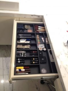 an open drawer on the side of a bathroom counter with makeup and toiletries in it