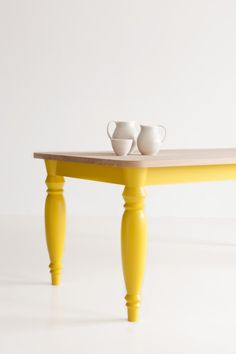 a yellow table with two cups on it and a white wall in the back ground