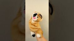 a hand holding a stuffed animal that looks like a cat with its paws on the wall