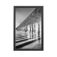 a black and white photo of a pier in the ocean with water reflecting off it