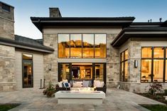 an outdoor fire pit in front of a large house with lots of windows and furniture