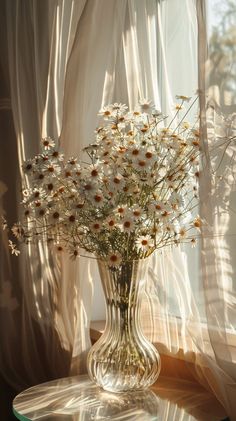 a vase filled with lots of white flowers on top of a table next to a window