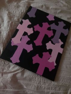 a black and pink canvas with crosses painted on it sitting on a white bed sheet