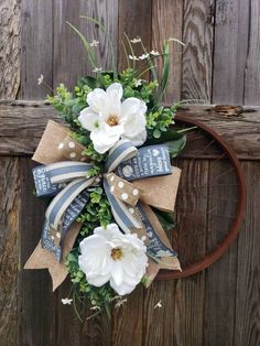 a wreath with white flowers and ribbon hanging on a wooden door frame in front of a fence