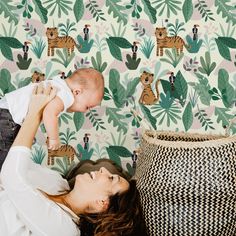 a woman holding a baby up to her face in front of a wallpapered background