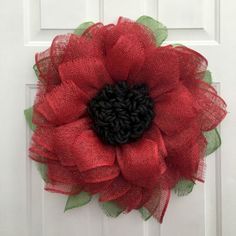 a red and green mesh wreath on a white door with a black center piece in the middle