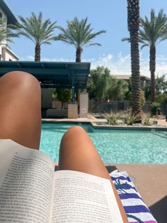 a person laying down next to a swimming pool with their feet on an open book