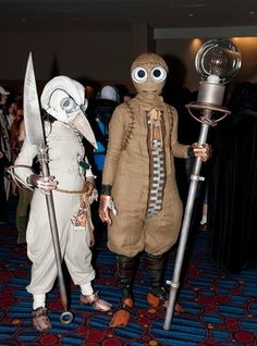 two people dressed in costumes and holding large metal poles, standing next to each other