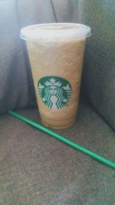 a starbucks drink sitting on top of a couch next to a green straw in a cup