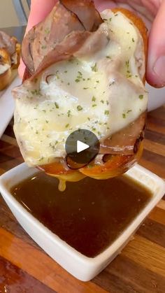 someone is holding up a sandwich with meat and cheese on it in front of some sauce