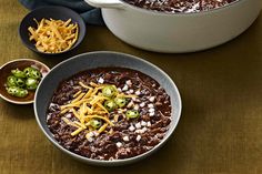 two bowls filled with chili and cheese on top of a brown table next to other dishes