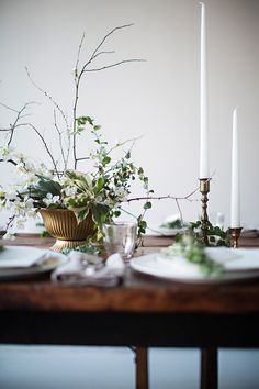 the table is set with white plates and silverware, greenery, and candles