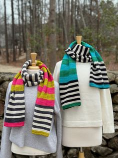 two knit scarves on mannequins in front of trees and stone wall