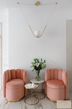 a living room with two pink chairs and a round table in front of a white wall