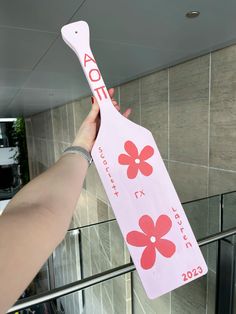 a person holding up a pink paddle with red flowers on it and the words aoe printed on it