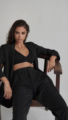 a woman sitting in a chair with her legs crossed, wearing black pants and a crop top