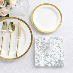 the table is set with white and gold plates, silverware, napkins, and flowers